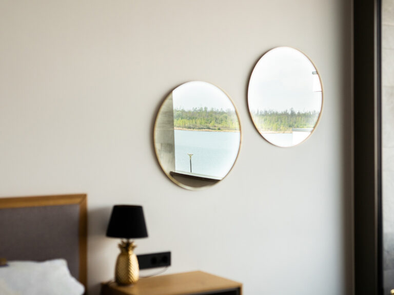 Das Bild zeigt einen Teil des Apartments 1 in Haus 14 (LAKESIDE). Zwei runde Spiegel im Schlafzimmer, in denen sich der See spiegelt.