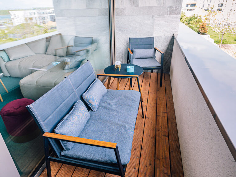 Das Bild zeigt den Balkon in Apartment 2 in Haus 14. Outdoor Sofa und Sessel sowie ein kleiner Beistelltisch mit Aschenbecher.
