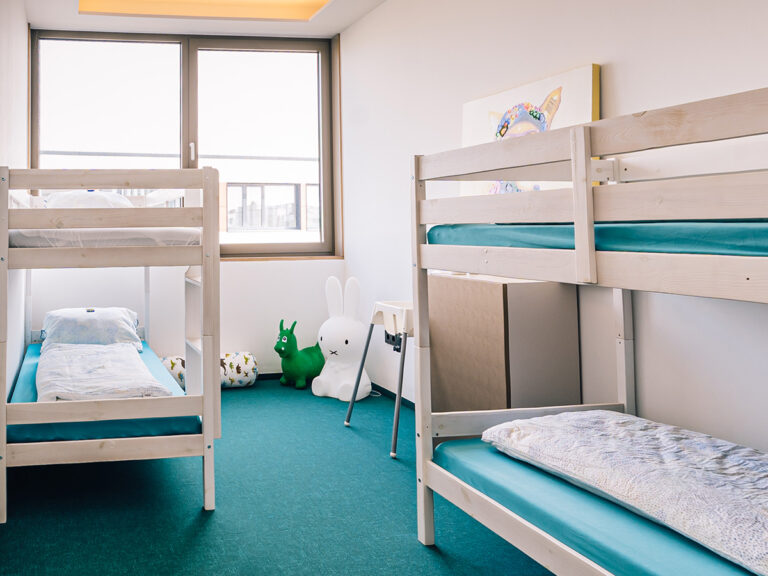 Das Bild zeigt das Kinderzimmer in Apartment 2. Zwei weiße Etagenbetten, petrolfarbener Teppich, helle Wände.