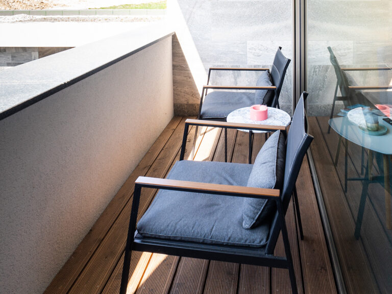 Das Bild zeigt den Balkon in Apartment 4. Holzdielen, zwei Sessel und Beistelltisch mit Aschenbecher.