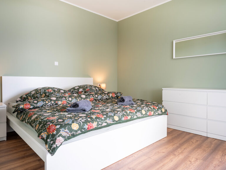 Schlafzimmer in Apartment 3 und 7 mit weißem Bett vor grünen Wänden.