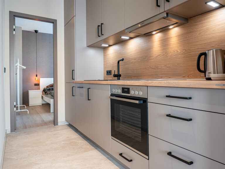 Küche in Apartment 2 in Haus 8: Durchgangszimmer mit Blick ins Schlafzimmer, graue Küchenmöbel mit Backofen.