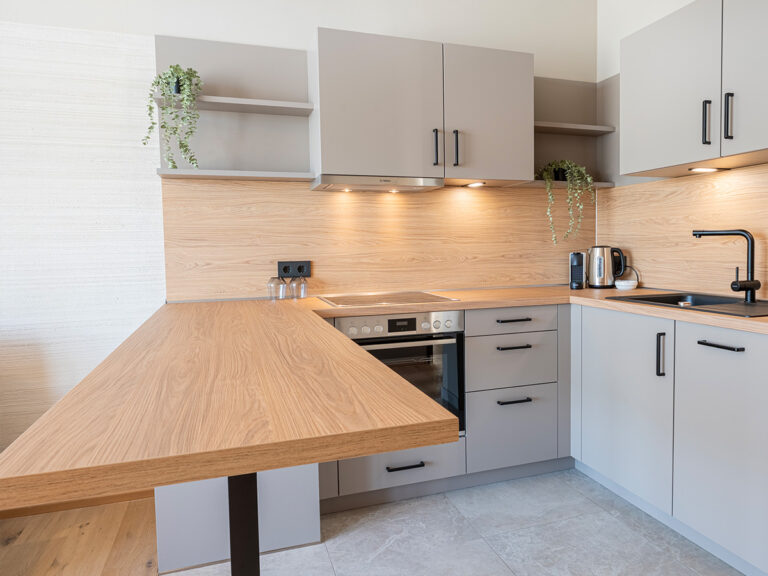 Offene Küche in Apartment 3 in Haus 8: graue Fliesen und Schränke, Holz-Arbeitsplatte und Tresen.