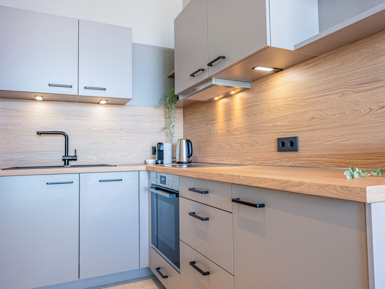 Offene Küche in Apartment 4 in Haus 8: graue Fronten, Wandspiegel und Arbeitsfläche in Holzoptik, Backofen.
