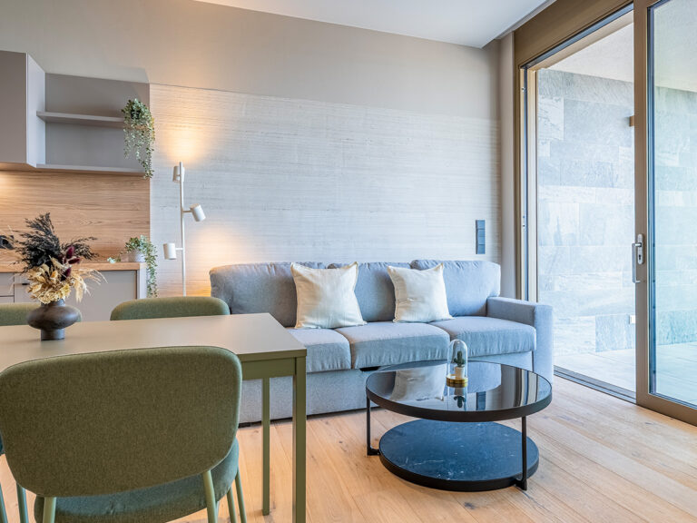 Wohnzimmer in Apartment 4 in Haus 8: Holzfußboden, grüne Sitzgruppe.